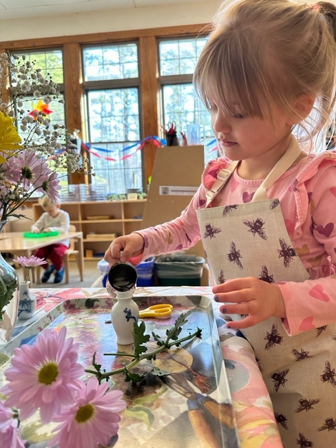 A child carefully pouring water into a vase during practical life work.